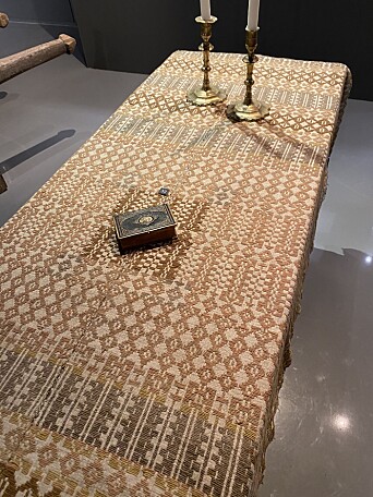 Åkle på kiste med salmebok og to lysestaker. Legg merke til "spegelen" som salmeboka ligger på. Bildet er fra utstillingen "Høgtider i livet" på Bø museum Åkle på kiste med salmebok og to lysestaker. Legg merke til "spegelen" som salmeboka ligger på. Bildet er fra utstillingen "Høgtider i livet" på Bø museum