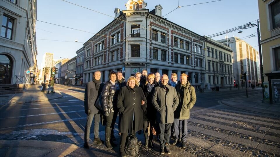 De står sammen om å realisere Pressens hus her, i Skippergata 22–26, som er hjørnet og kvartalet i bakgrunnen. Foran: Elin Floberghagen, NP; bak henne fra venstre utleiemekler Stig Wadahl; Torill Roås, MBL; Bård Idås, NTB; Per Brikt Olsen, Fagpressen; Eivind Fjellstad, IJ; Randi Øgrey, MBL; Arne Jensen, NR; Mads Yngve Storvik, NTB; Geir K. Hus, LLA og Kristoffer Egeberg, Faktisk.no. (Foto: Håkon Mosveen, NTB).